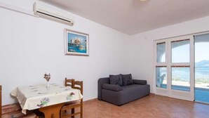 A dining area with a table and chairs, a gray sofa, a painting on the wall, and a view through large windows. - Spacious and Cozy Seafront Apartments (Ston)