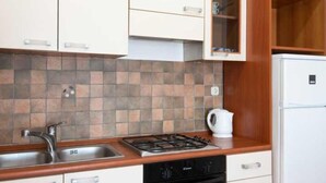 A kitchen with white cabinets, a tiled backsplash, a gas stove, a sink, and a white refrigerator. - Spacious and Cozy Seafront Apartments (Ston)