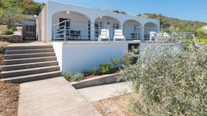 A modern building with a flat roof, a covered outdoor seating area with chairs, and a staircase leading to the entrance. - Spacious and Cozy Seafront Apartments (Ston)