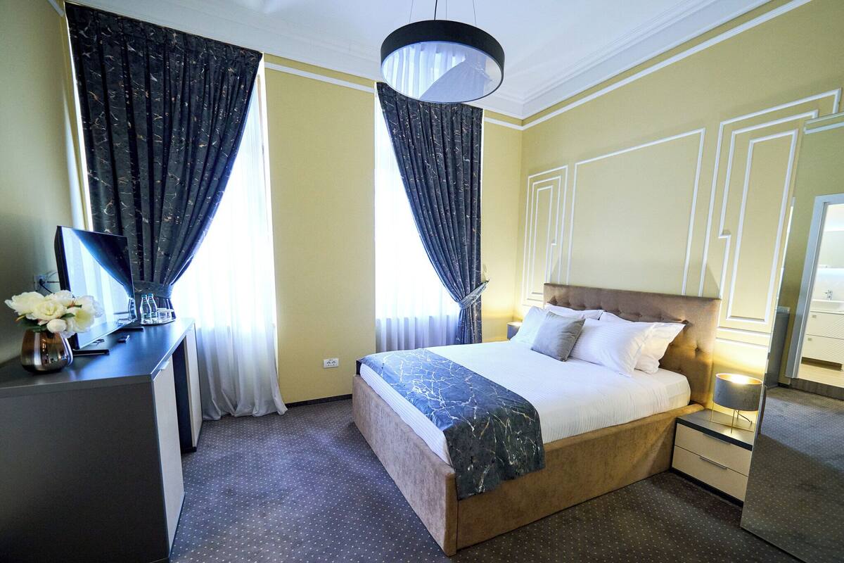Une chambre d’hôtel avec un grand lit, un bureau agrémenté d’un vase de fleurs et des rideaux aux fenêtres.