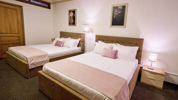A hotel room with two beds, a wooden wardrobe, a bedside table with a lamp, and a framed picture on the wall.