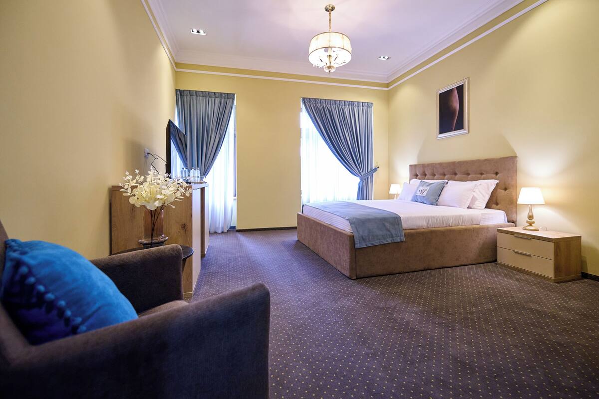 Une chambre d’hôtel avec un grand lit, une table de chevet avec une lampe, une chaise et un vase de fleurs.