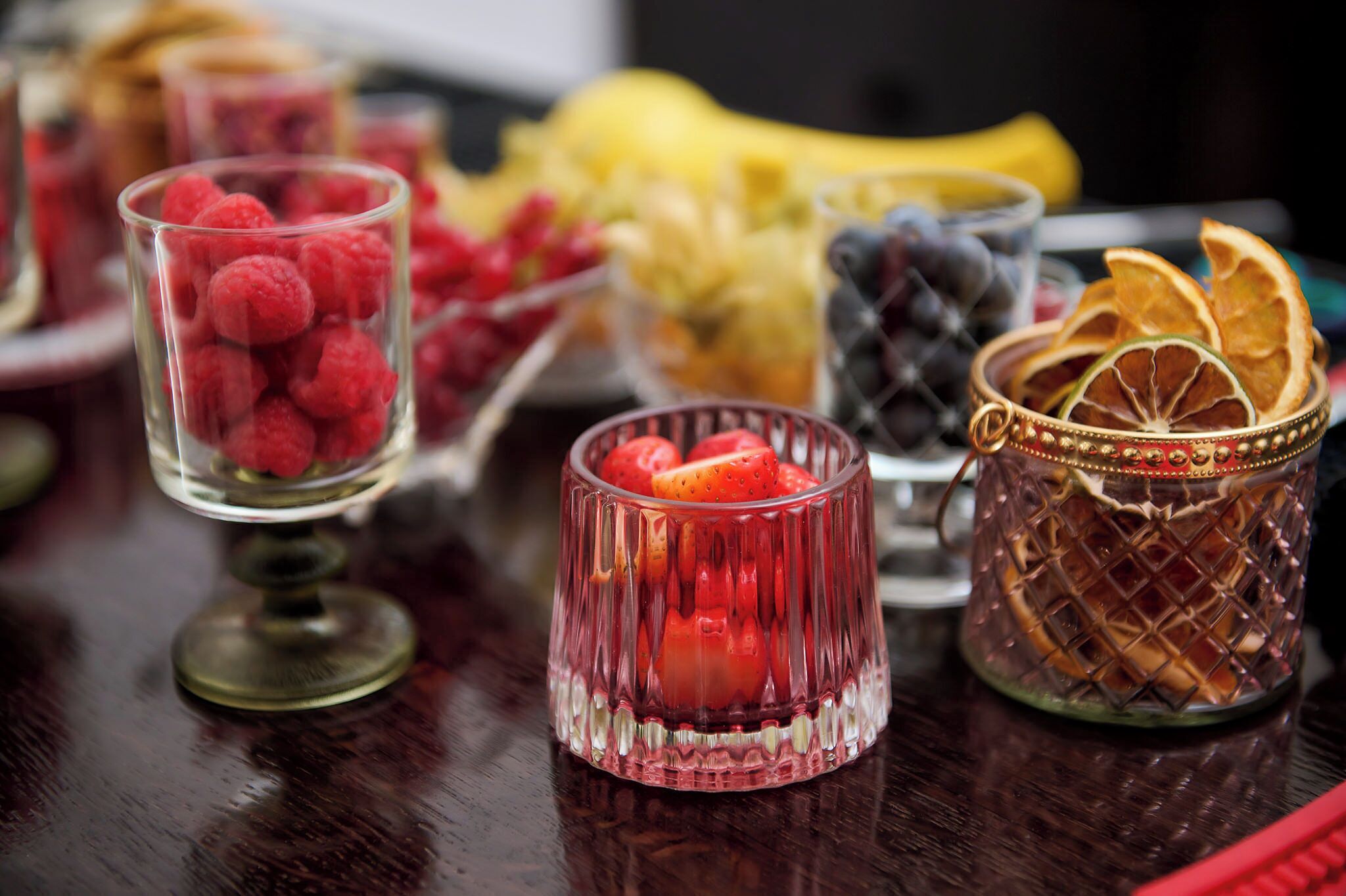 A table with various food items including raspberries, strawberries, and dried fruits in decorative glass containers.