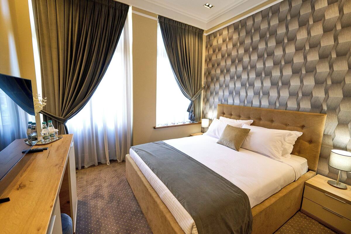Une chambre d’hôtel avec un grand lit, un bureau en bois, un téléviseur à écran plat et une fenêtre avec des rideaux.