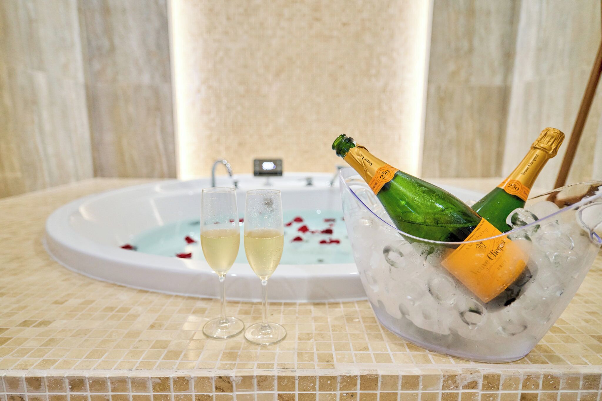 Een bad gevuld met ijs en champagneflessen, twee champagneglazen en rozenblaadjes die in het water drijven.