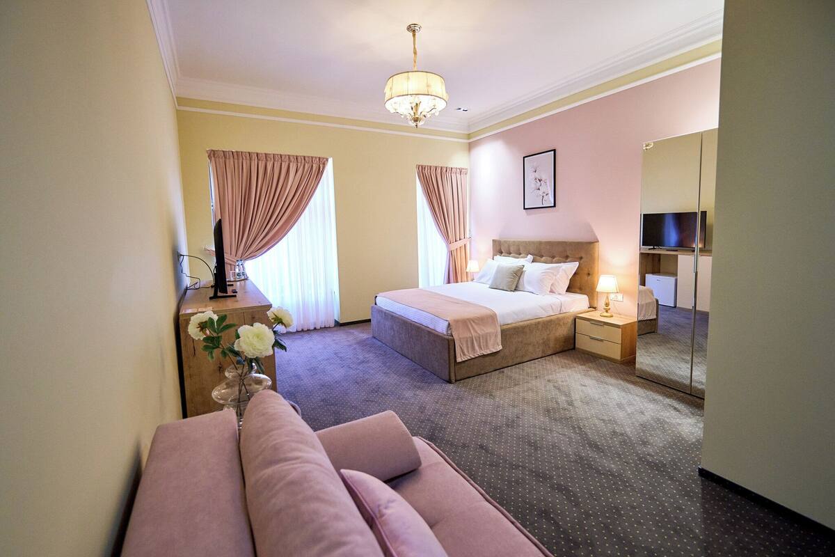 Une chambre d’hôtel comprenant un lit, une table de chevet, une lampe, un miroir et un banc avec des coussins.