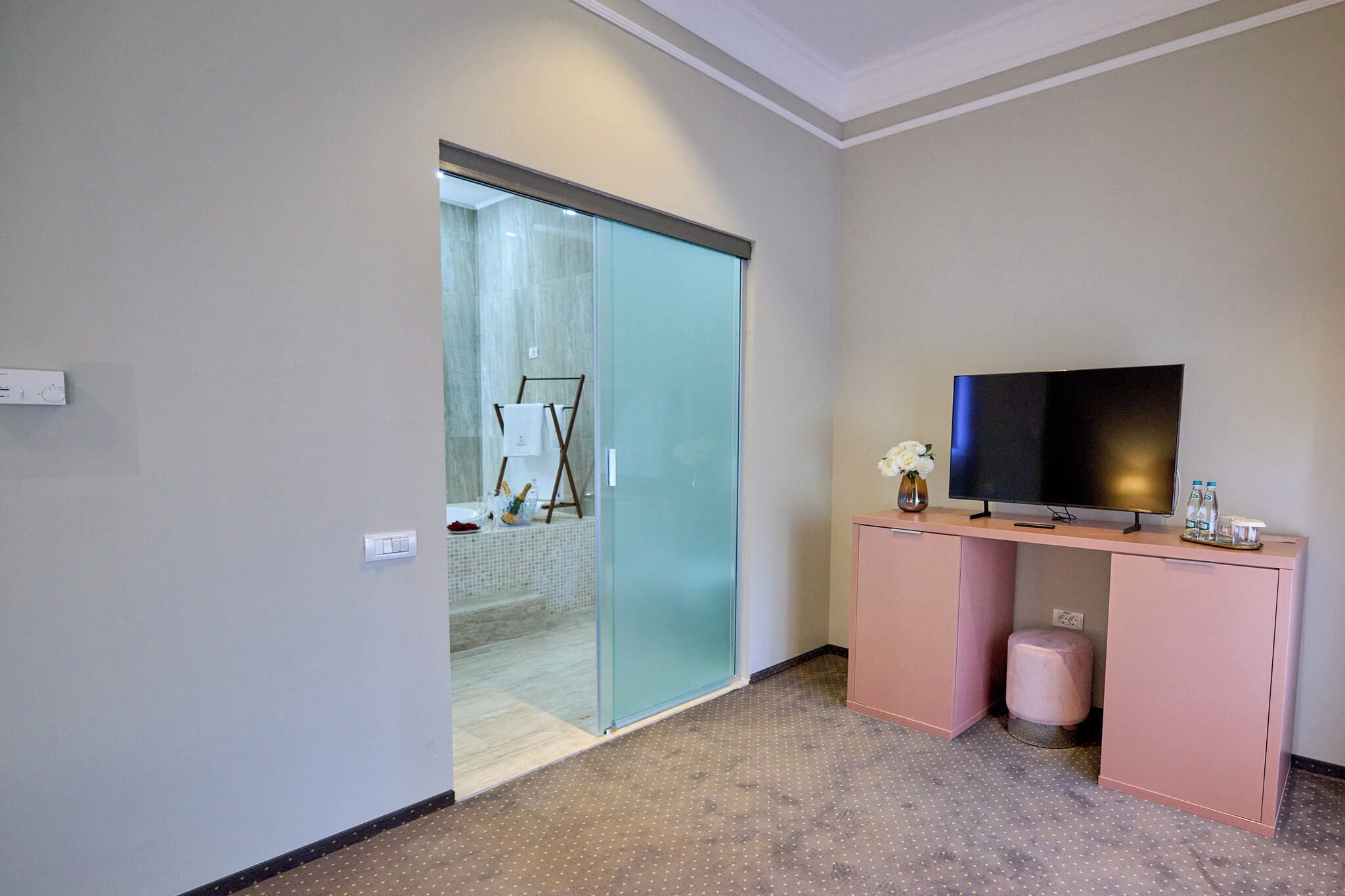 Ein Hotelzimmer mit einer Schiebetür zu einem Badezimmer, einem Flachbildfernseher auf einem rosa Schrank und einem kleinen Hocker.