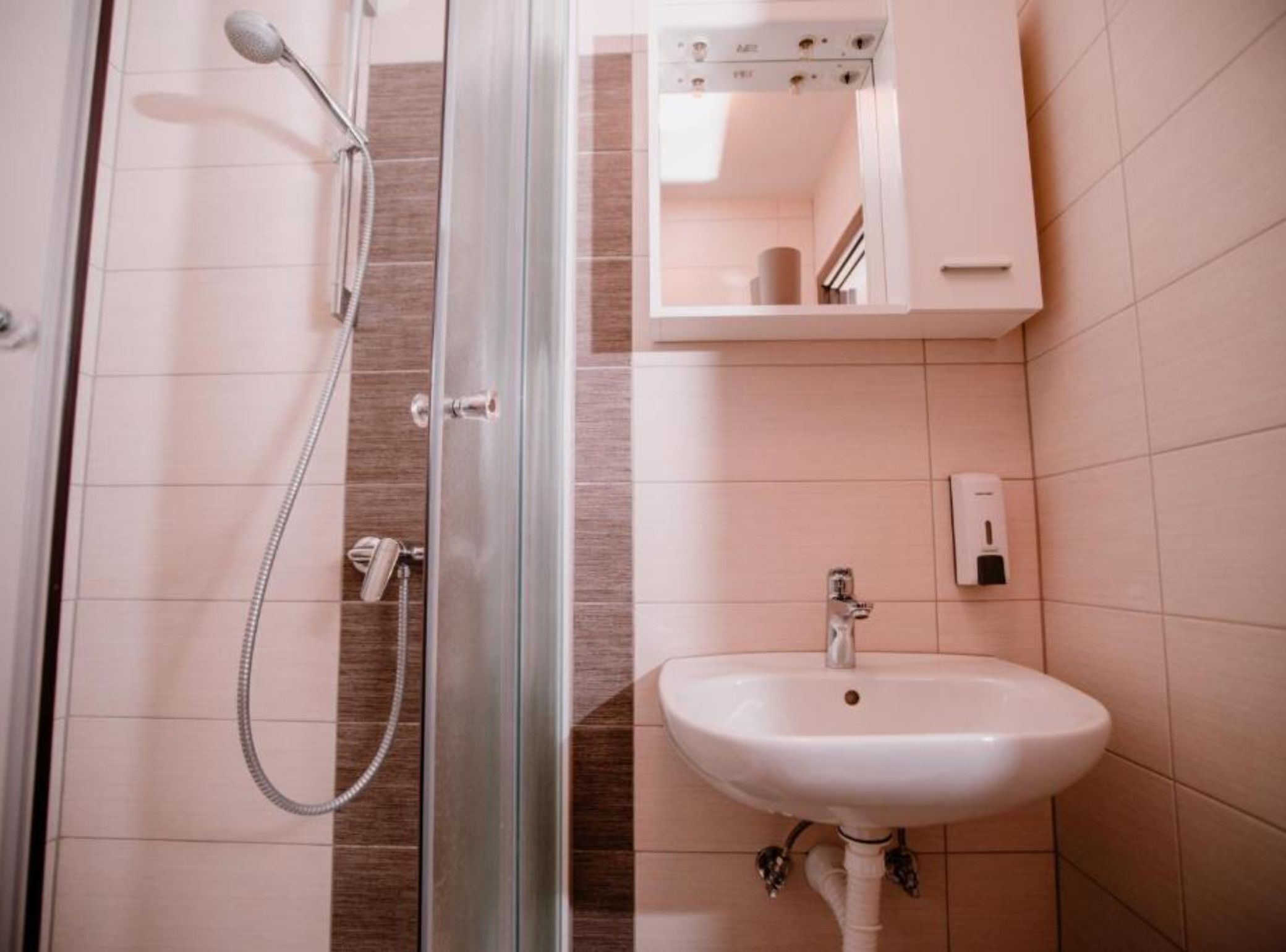 A modern bathroom with a glass shower enclosure, a white sink, and a small cabinet with toiletries.