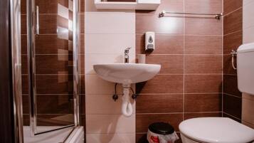 A bathroom with a glass shower enclosure, a white sink, a toilet, and a towel rack.