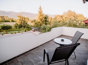 A rooftop terrace with a round table and chairs, surrounded by a white wall and a view of trees and mountains. - Mountain Serenity Rooms (Plitvicka Jezera)