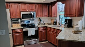 A modern kitchen with wooden cabinets, stainless steel appliances, and a marble countertop.
