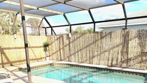 A swimming pool with a covered area, lounge chairs, and a wooden fence.