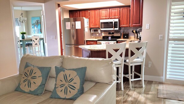 A living room with a beige sofa, a dining area with a table and chairs, and a kitchen with wooden cabinets and modern appliances.