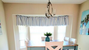 A dining area with a wooden table and chairs, a chandelier, and a window with blinds.