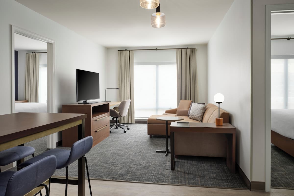 Habitación de hotel con escritorio, televisión, sofá y vistas al exterior.