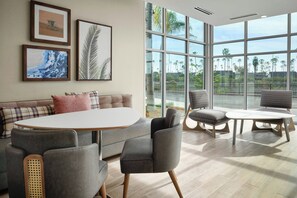 A modern living room with a sofa, two armchairs, a round table, and large windows offering a view of palm trees. - Residence Inn by Marriott Ventura Beach (Ventura)