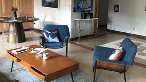 Un salon moderne avec une table basse en bois, deux fauteuils bleus, un canapé bleu et un coin repas comprenant une table ronde et des chaises.