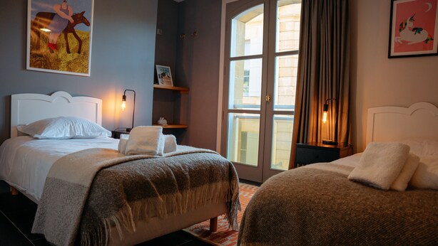 Une chambre d’hôtel avec deux lits, une grande fenêtre, une table de chevet et un mur décoré d’œuvres d’art.