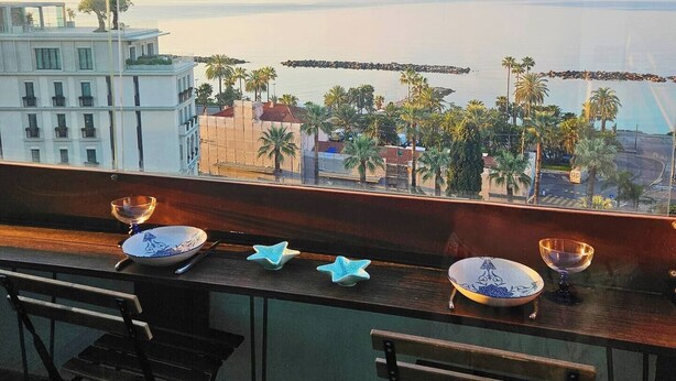 Ein Balkon mit Meerblick, eine Holzbank und ein Esstisch mit Tellern und Schüsseln.
