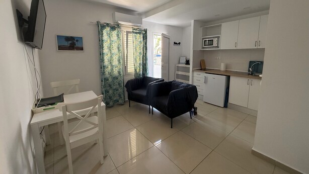 A compact living space with a kitchenette, a dining area with a white table and chairs, and a black sofa. - Balcony Studio Vacation Home (Unknown)