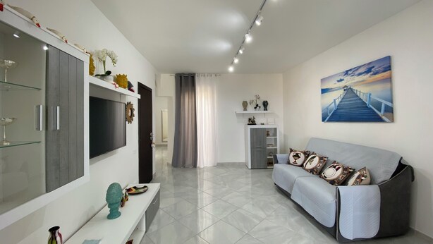 A modern living room with a flat-screen TV, a sofa, a coffee table, and a painting of a pier. - Pearl Diva Apartment (Palermo)