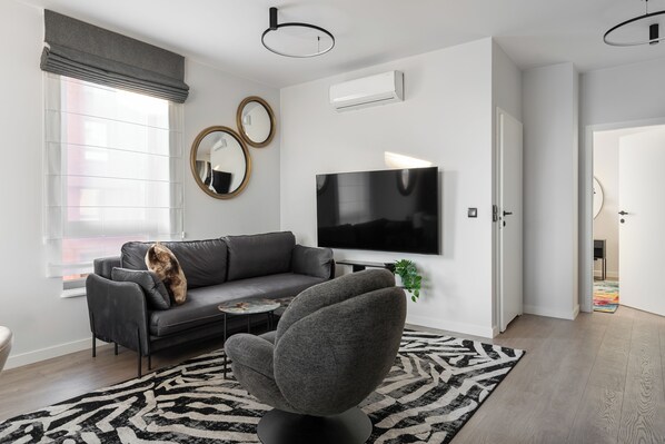 A modern living room with a grey sofa, a black armchair, a flat-screen TV, and a patterned rug.