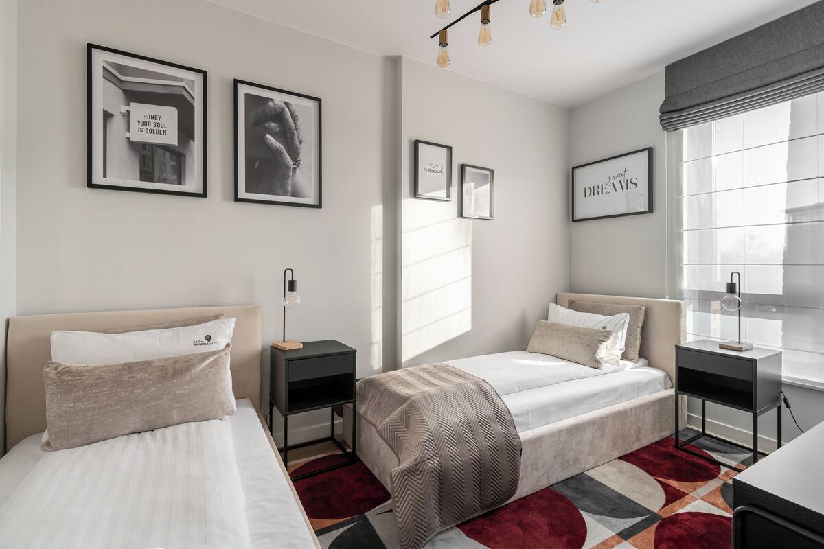 Ein modernes Hotelzimmer mit zwei Betten, einem großen Fenster mit Jalousien und gerahmten Kunstwerken an den Wänden.