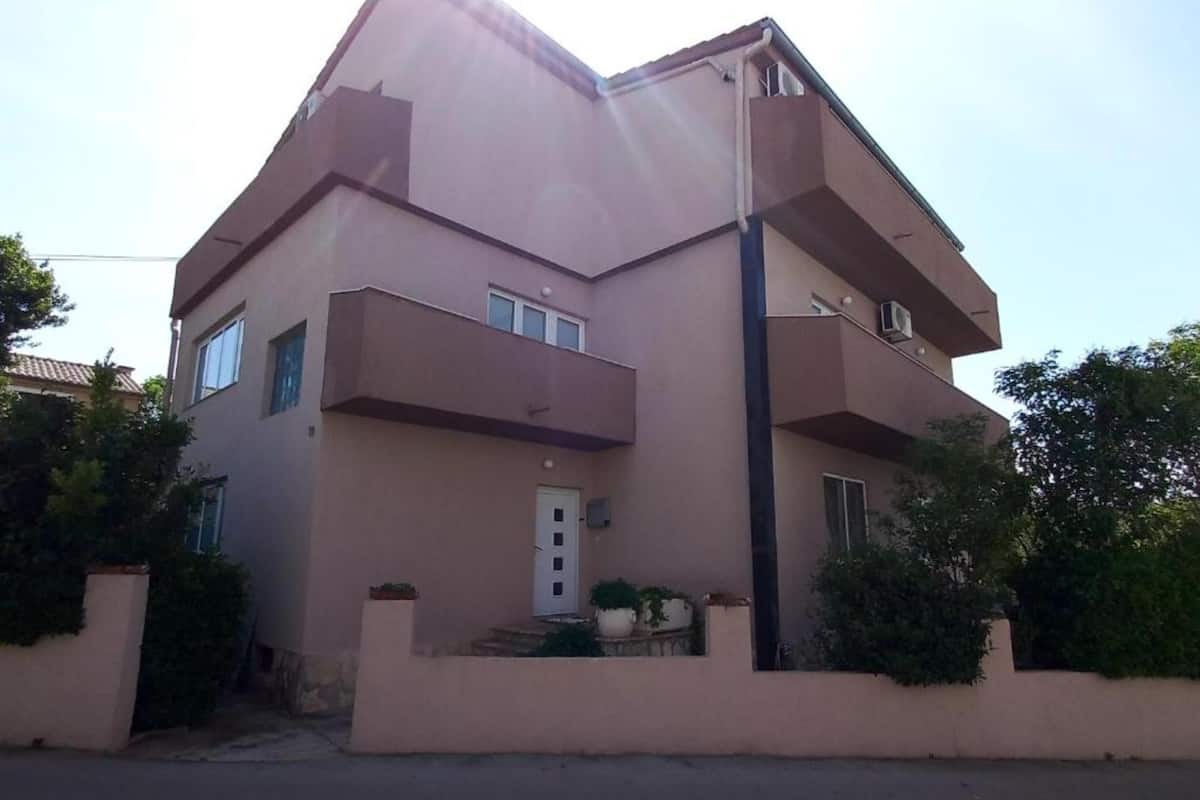 A two-story building with a flat roof, a central entrance, and a small porch with potted plants.