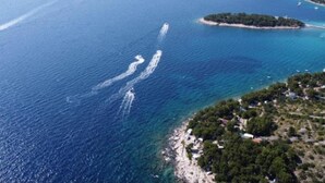 An aerial view of a coastal area with clear blue waters, several small islands, and a densely vegetated shoreline. - Pansion Stones Murter (Murter-Kornati)