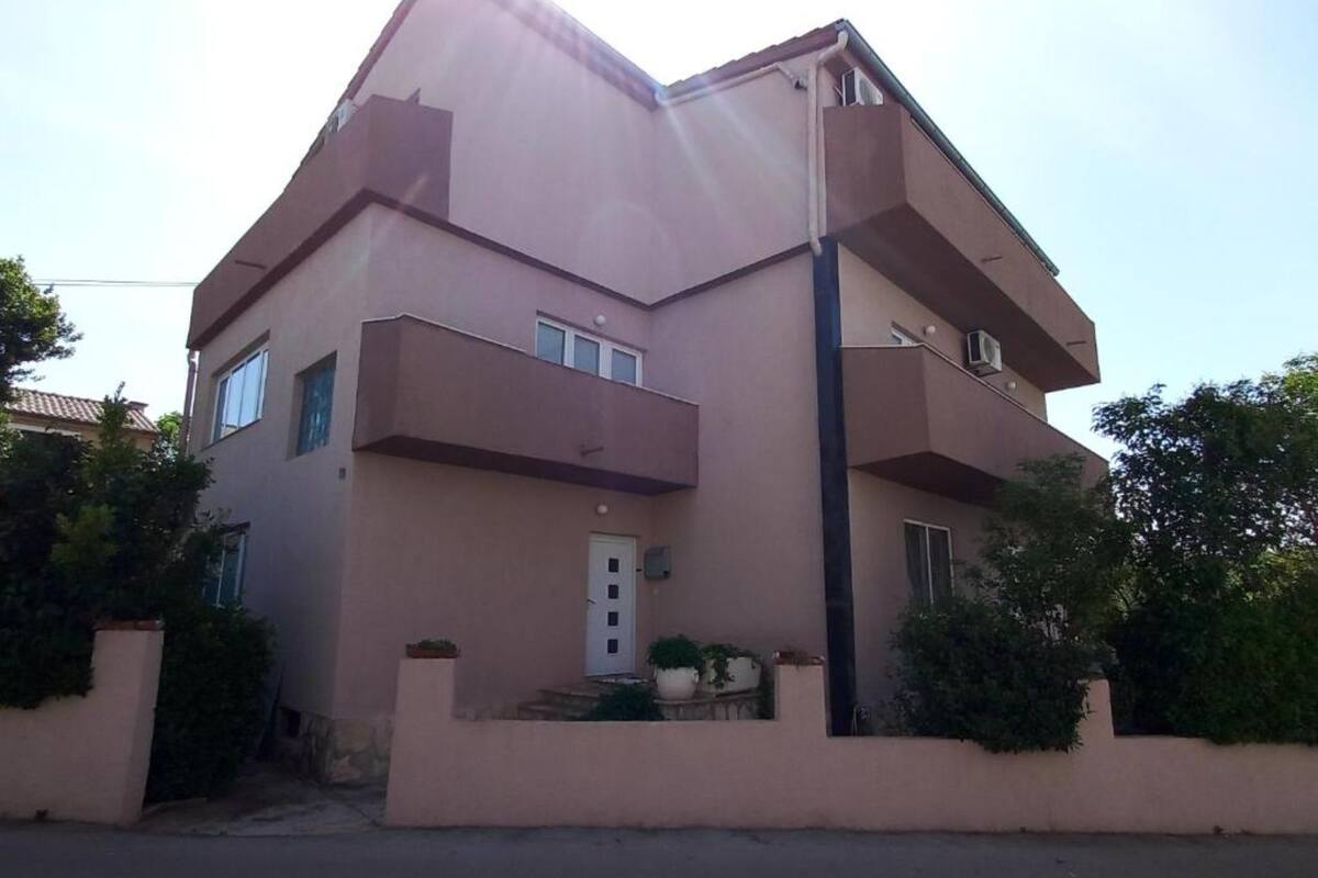 A two-story building with a flat roof, a central entrance, and a small porch with potted plants.