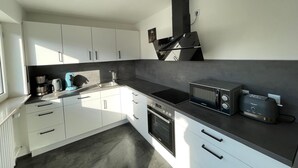 A modern kitchen with white cabinets, a black countertop, a built-in oven, a microwave, and a toaster. - Vacation apartment Taubersonne (Igersheim)