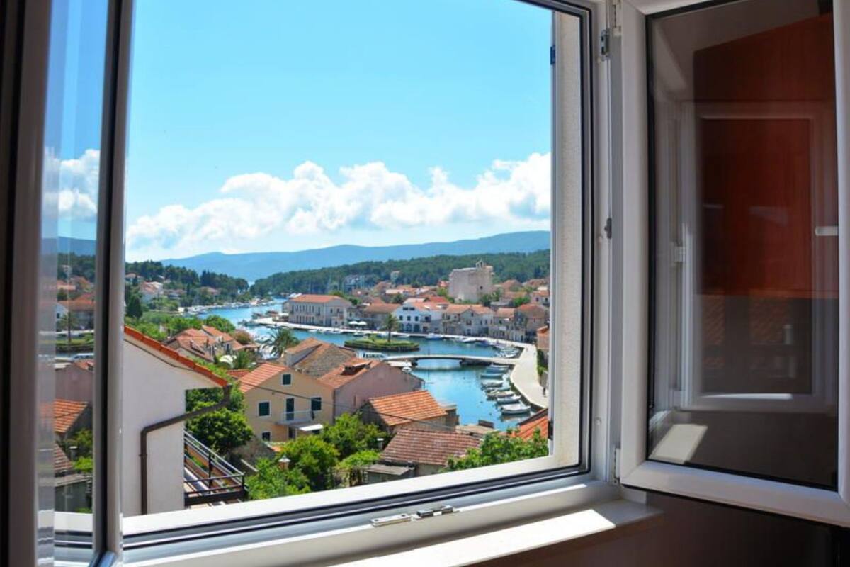A window with a view of a town by a river, buildings, and mountains in the distance.
