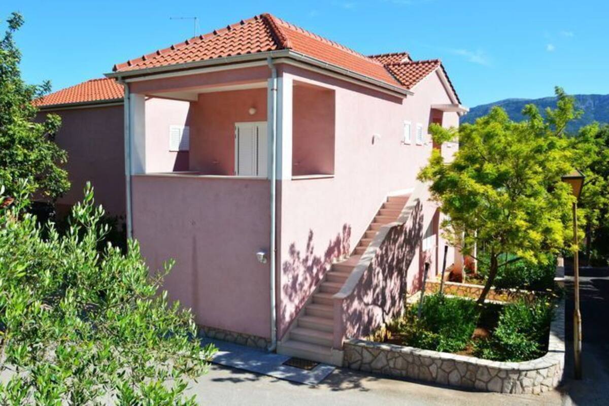 A pink villa with a red-tiled roof, a covered porch, and a stone staircase leading to the entrance.