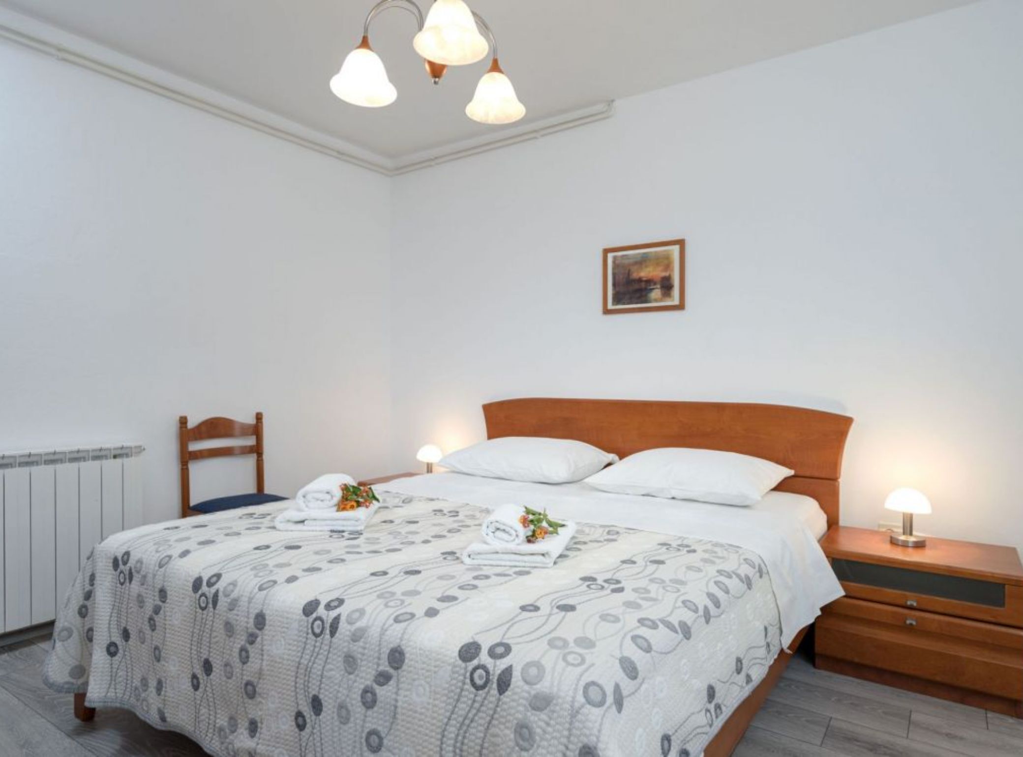 Ein Schlafzimmer mit Bett, Nachttischen, einem Holzkopfteil, einem Gemälde an der Wand und einer Deckenleuchte.