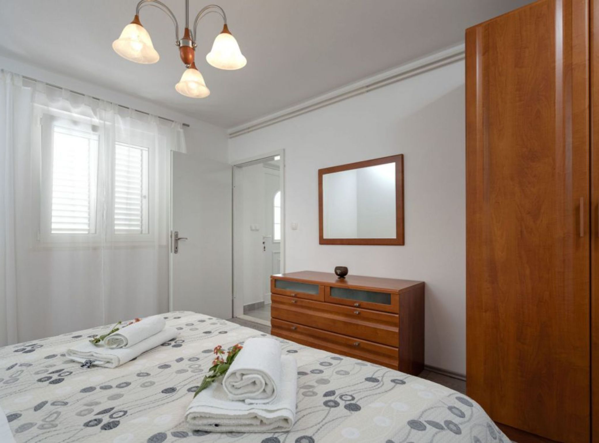 Ein Schlafzimmer mit einem Bett, einer Holzkommode, einem Spiegel und einer Tür.