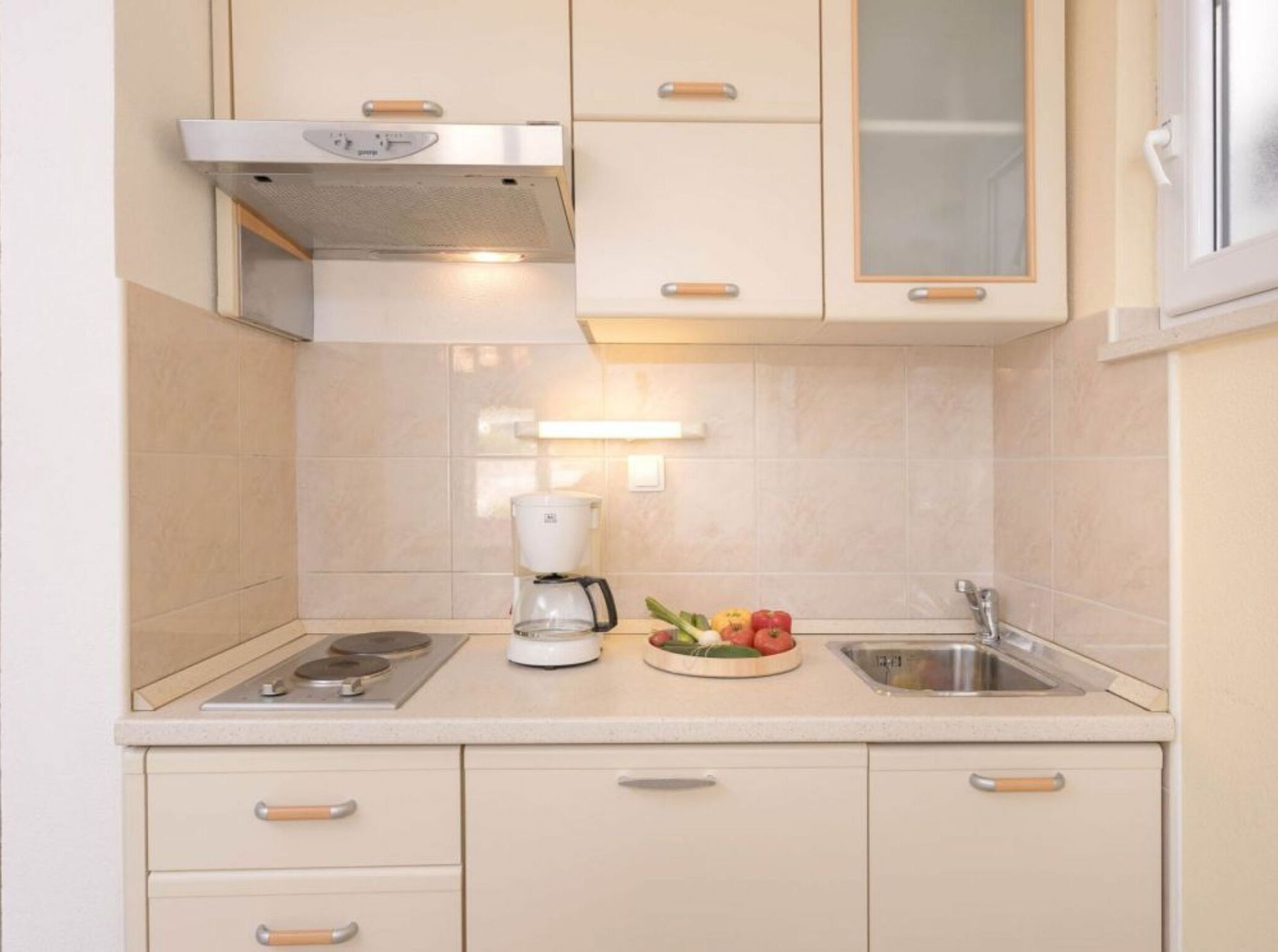 A compact kitchen with a stove, coffee maker, and a fruit bowl on the counter.