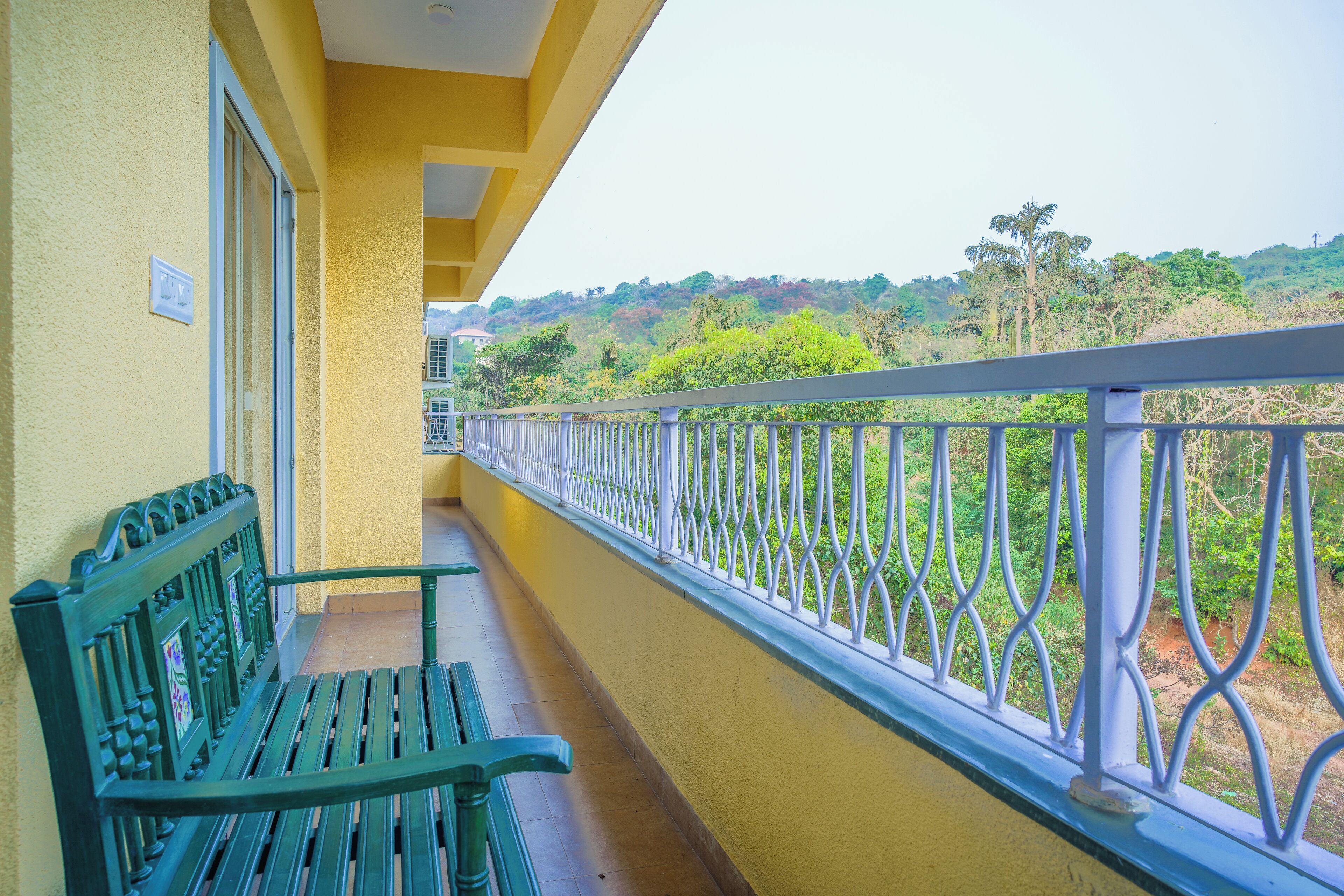 Un balcón con un banco verde y vistas a un paisaje verde exuberante.