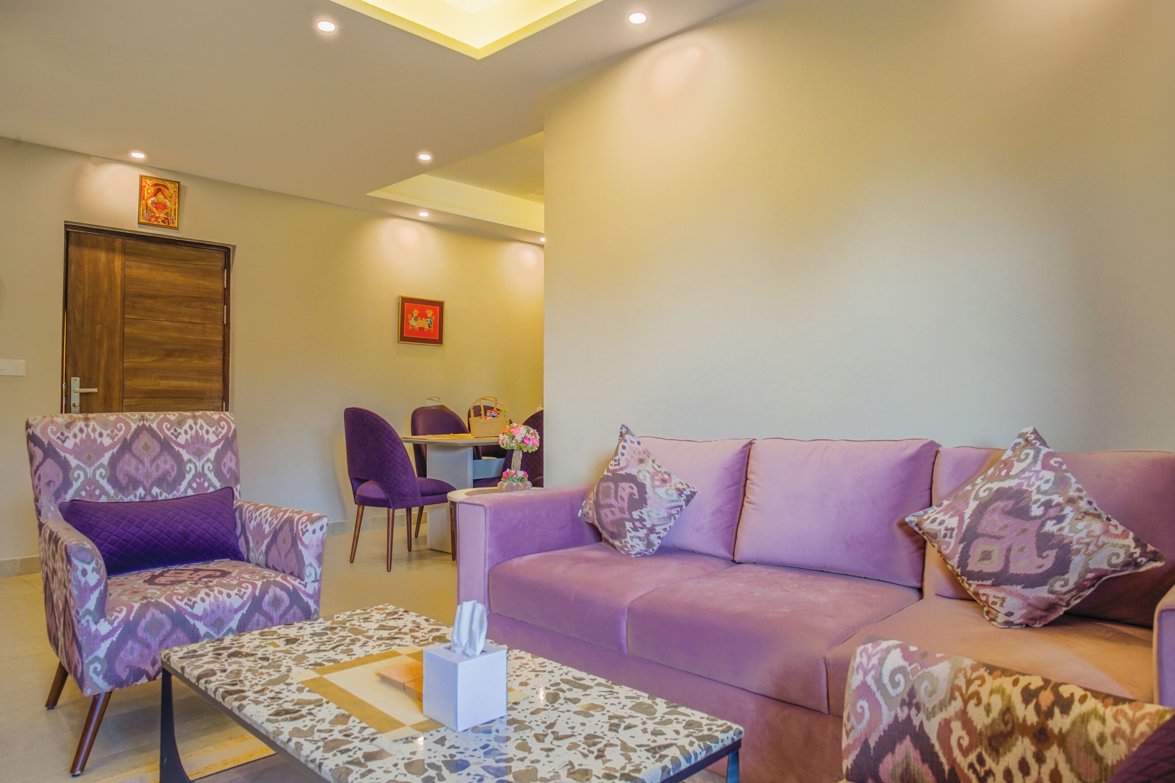 Un salon avec un canapé violet, un fauteuil à motifs et une table basse.