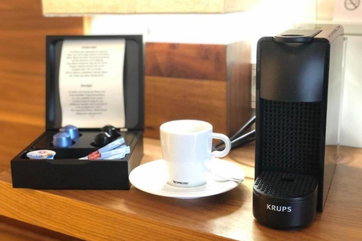 Una cafetera, una taza de café y una caja con manual sobre una mesa de madera.