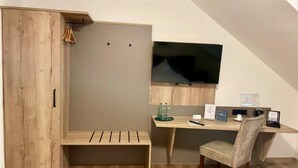 A room with a wooden wardrobe, a desk with a chair, a flat-screen TV mounted on the wall, and a bench. - Hotel Fliederbusch  (Borken)