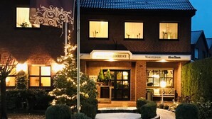 A hotel with a brick facade, a signboard with the name 'Hotel Haus Fliederbusch', and a well-lit entrance. - Hotel Fliederbusch  (Borken)