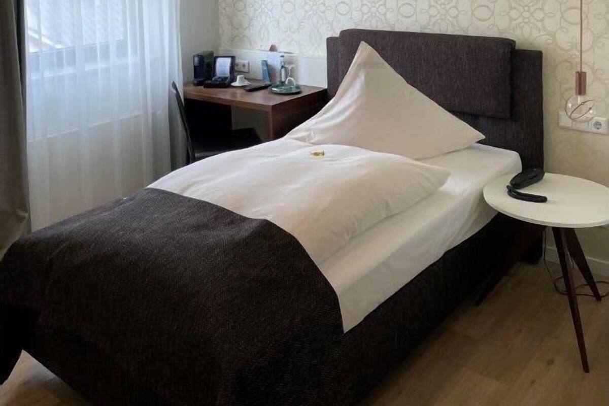 Habitación de hotel con cama, escritorio, silla, mesita y ventana con cortinas.