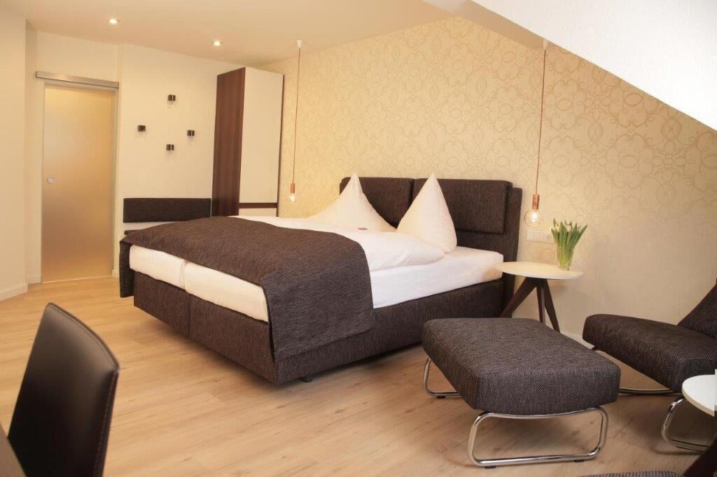 A modern bedroom with a large bed, a small table with a plant, and two chairs.