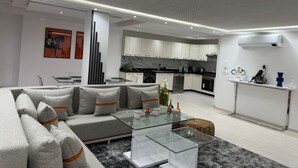 Un saló modern amb un sofà modular, una taula de centre de vidre i una cuina al fons.