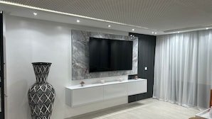 Un saló modern amb una paret de marbre, un televisor pla gran, una taula de consola blanca i un vas decoratiu blanc i negre.