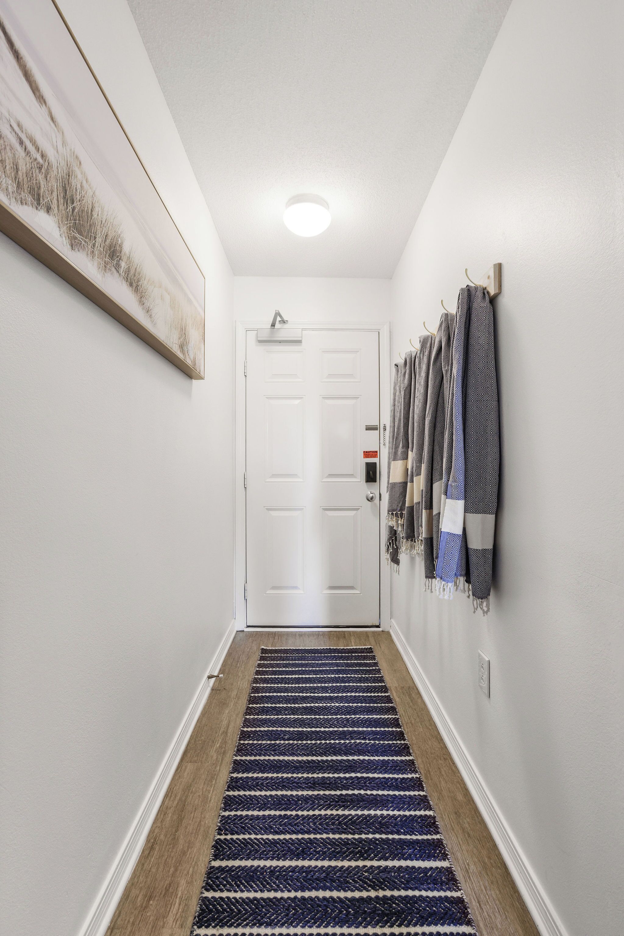 Een gang met een witte deur, een zwart-blauw gestreept tapijt en een rij sjaals aan de muur.