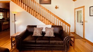 A living room with a wooden staircase, a black leather sofa with patterned cushions, a dining table, and a kitchen area in the background. - Wilderness Ridge - Starry Nights & Mountain Sights - Pet Friendly (Sevierville)