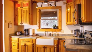 A kitchen with wooden cabinets, a sink, a stove, and a window with a view of trees. - Wilderness Ridge - Starry Nights & Mountain Sights - Pet Friendly (Sevierville)