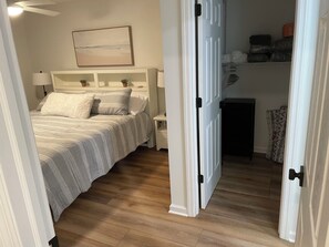 Een slaapkamer met een bed, nachtkastjes, een plafondventilator, een schilderij en een deur naar een andere kamer.