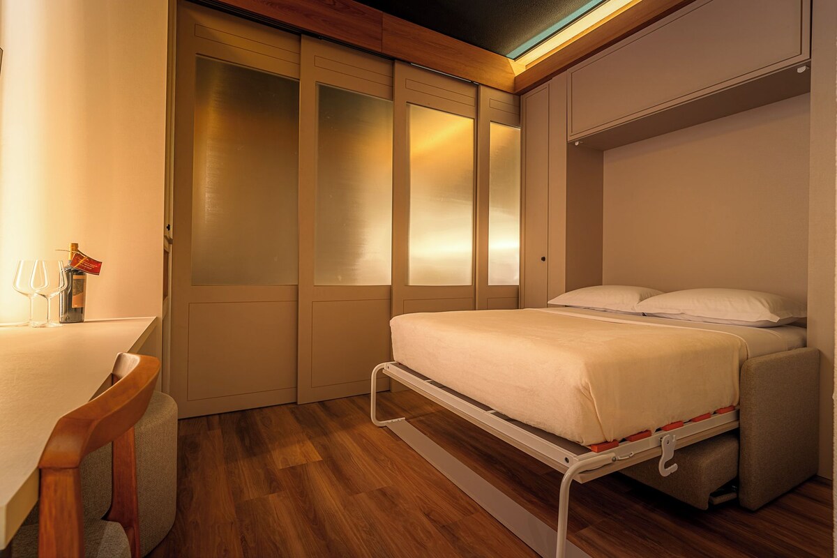 Un dormitorio pequeño con cama, mesita de noche y un rincón de descanso.